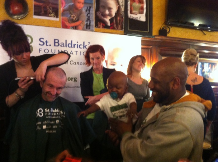 Jim McKeever, author of the blog Irish Investigations, enjoys the finishing touches of his head shaving today, as the child he chose to honor, Arie, watches in the arms of her father.